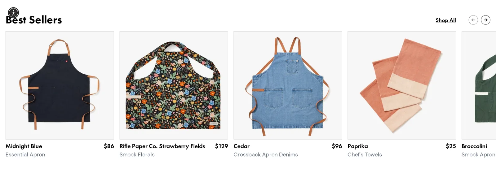Hedley & Bennett homepage Best Sellers row with a Midnight Blue Essential Apron at $86, a Rifle Paper Co. Strawberry Fields Smock at $129, a Cedar Crossback Apron at $96, Paprika Chef's Towels at $25 and a Broccolini Smock Apron