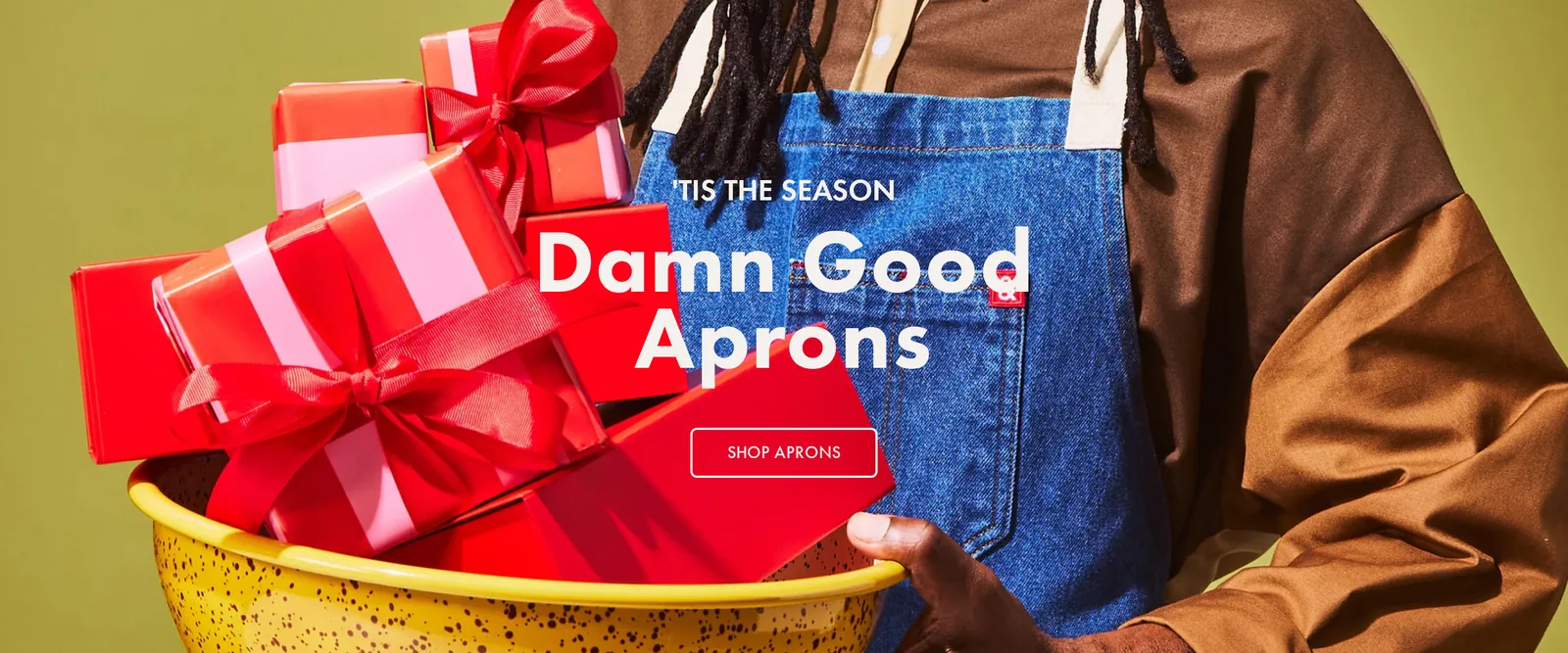 Hedley & Bennett homepage hero with a person in a blue apron holding wrapped gifts in a yellow bowl, under the words Damn Good Aprons and a Shop Aprons button